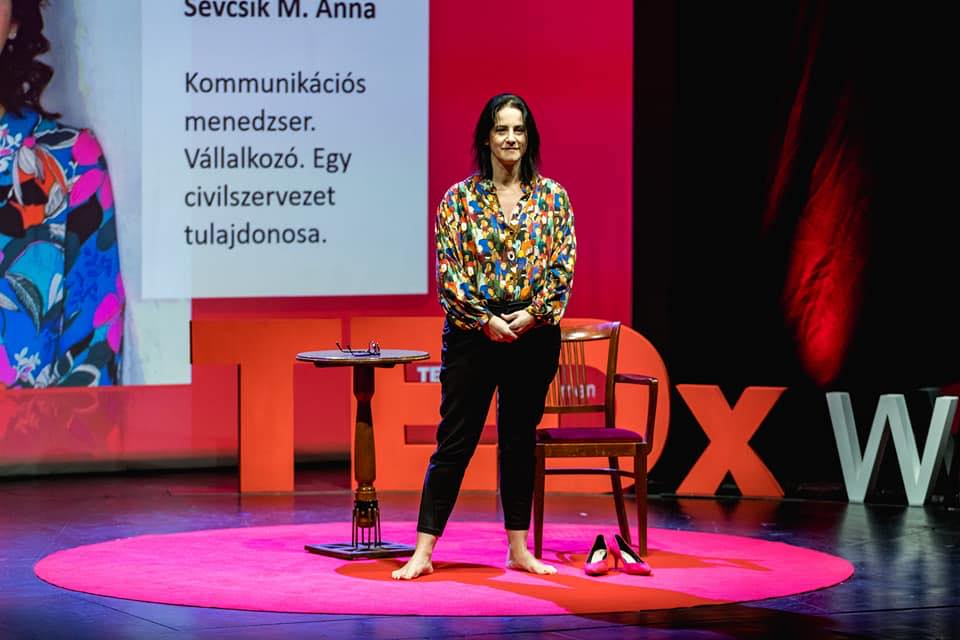 Anna M Sevcsik is standing on the stage of TEDx with the help of buriba